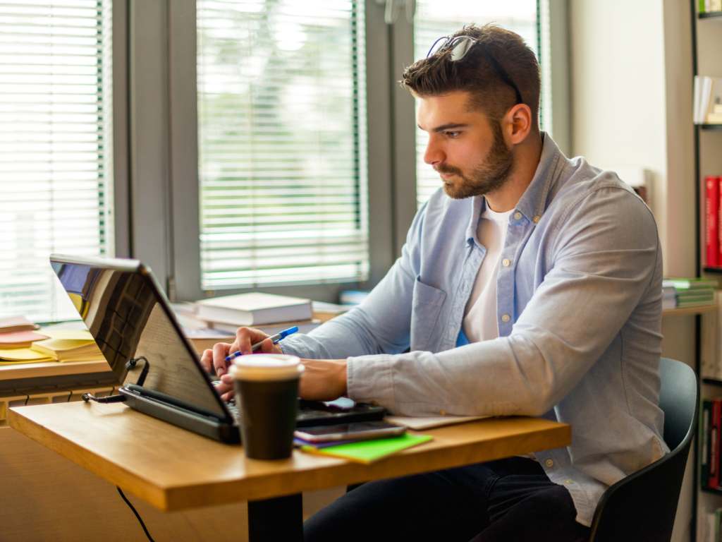Investigación digital para el marco contextual de tesis Estudiante investigando el marco contextual de su tesis en laptop en biblioteca.