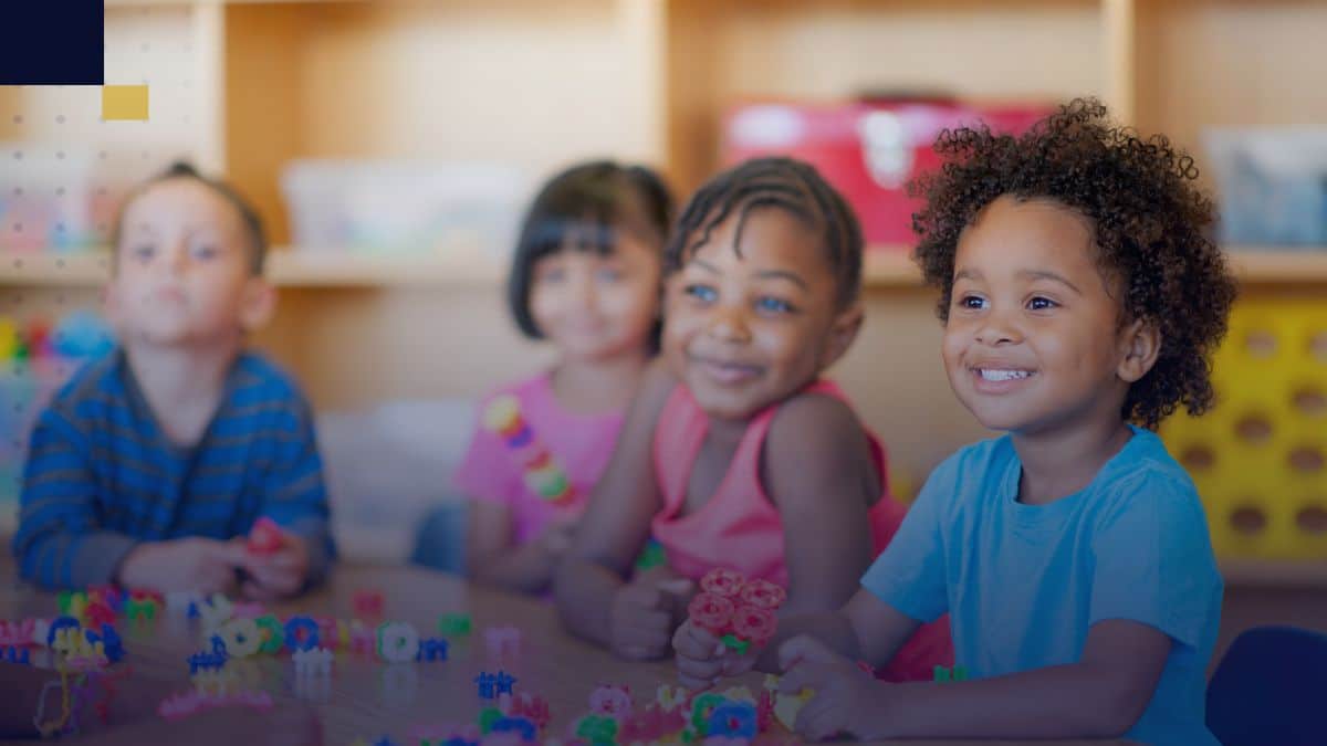 Grupo de niños pequeños sentados en mesa de aula, participando en actividades de aprendizaje y socialización en el nivel de educación inicial.