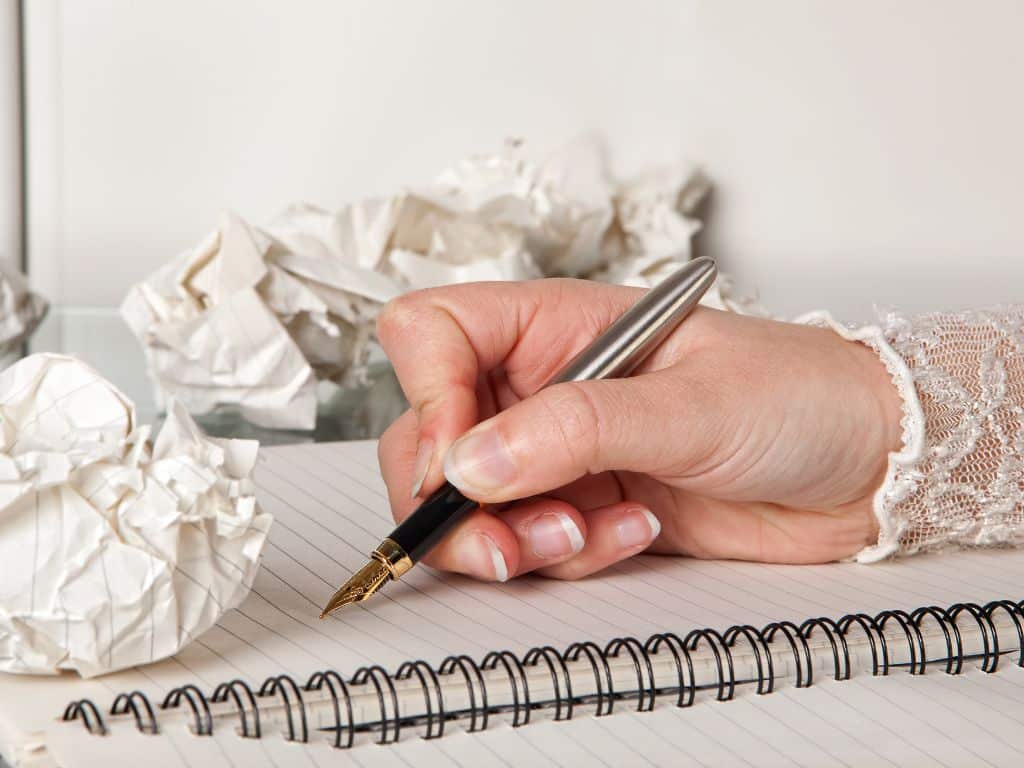 Escritura y revisión de ensayos con conectores adecuados Persona redactando ensayo y corrigiendo conectores textuales en borradores