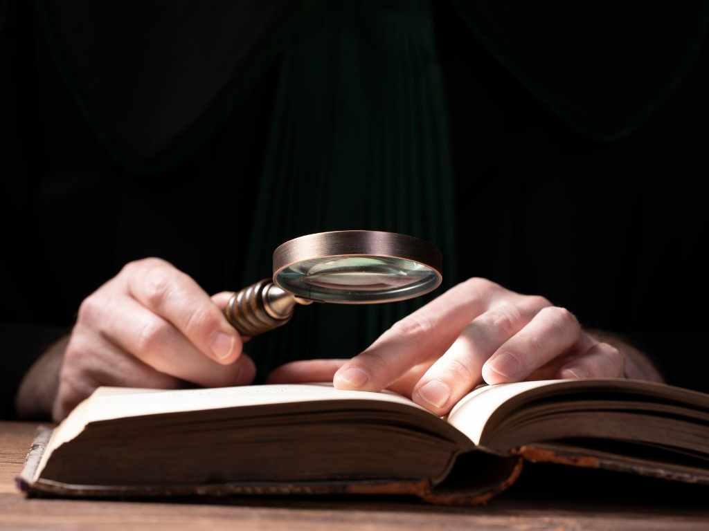 Análisis bibliográfico en Derecho Penal para tesis Investigador jurídico analizando libro de derecho penal con lupa.