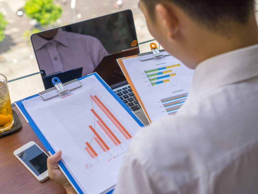 Investigación correlacional: análisis de gráficos y datos para medir la relación entre variables Persona analizando gráficos y tablas de datos estadísticos impresos, con laptop y móvil, para interpretar la relación entre variables en una investigación correlacional.