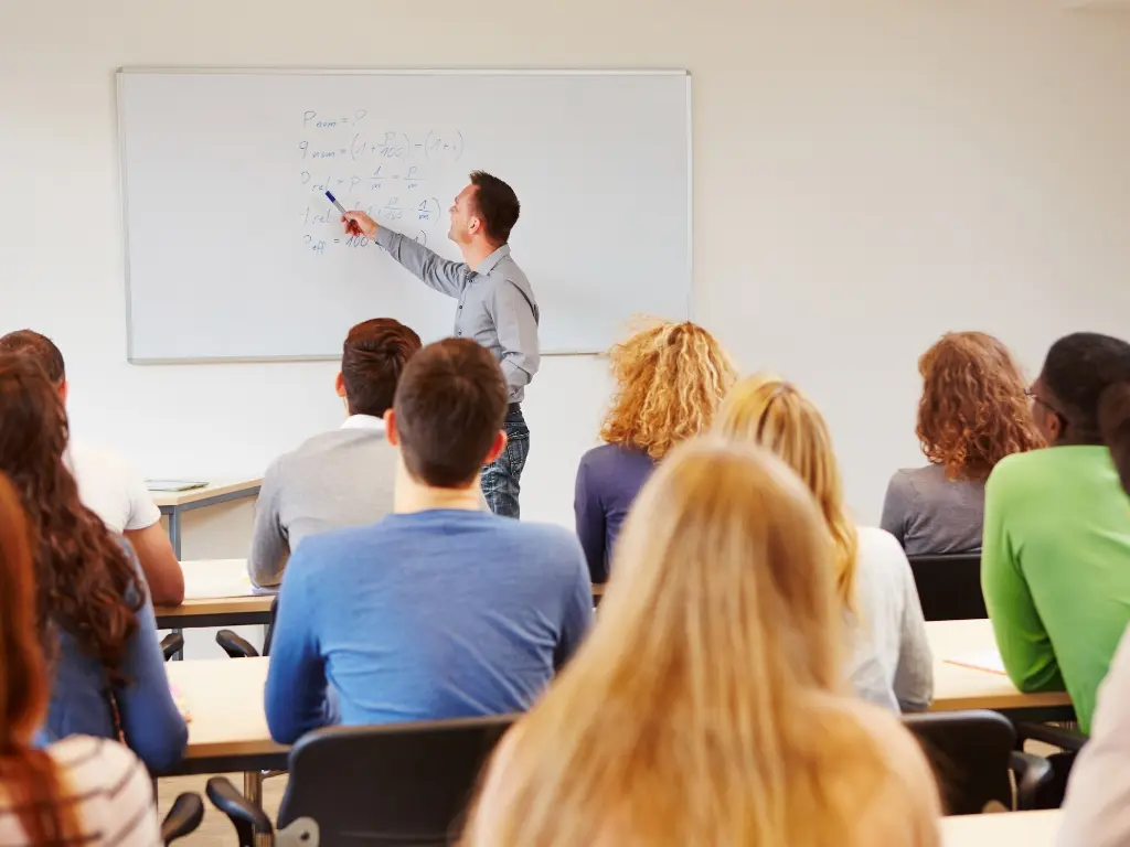 Doctorado en Educación: docente explicando teoría e investigación a estudiantes de posgrado Docente universitario explicando conceptos en el tablero a un grupo de estudiantes de posgrado en un aula de clase.