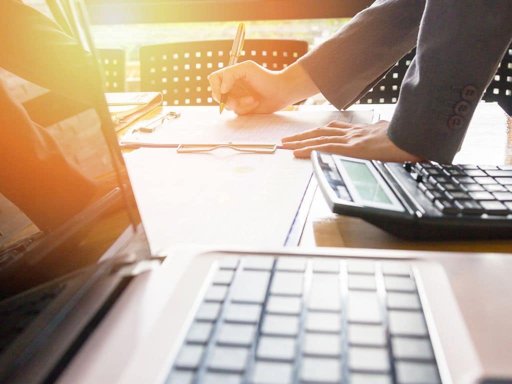 Tesis de Administración Financiera: análisis de gráficos y datos económicos para el proyecto académico Mano de estudiante analizando gráficos financieros en tablet y papel, realizando cálculos y anotaciones para una tesis de Administración Financiera.