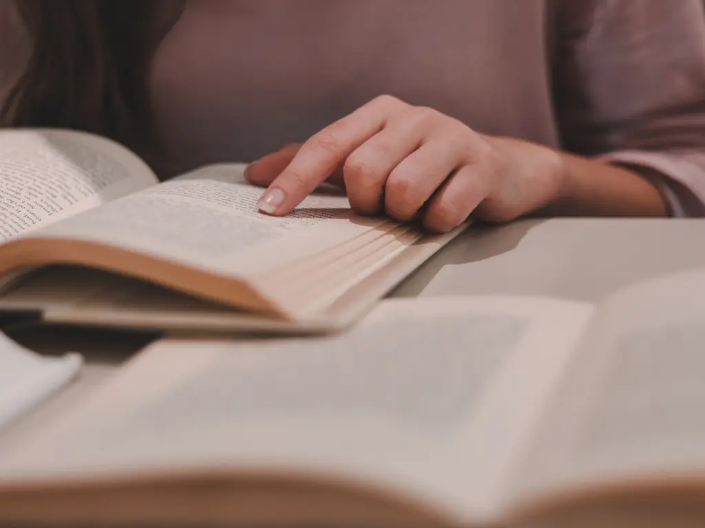 Elaboración de fichas bibliográficas: estudiante revisando libros y seleccionando información relevante Mano de estudiante señalando información relevante en un libro abierto, durante la consulta de fuentes para elaborar fichas bibliográficas.