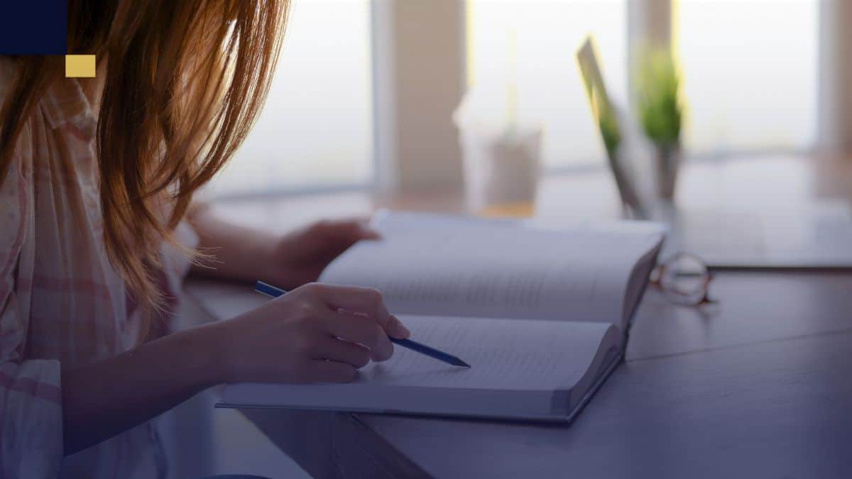 Estudiante universitaria revisando y subrayando información en un libro, comparando características y estructura de tesis y tesina para su proyecto académico.