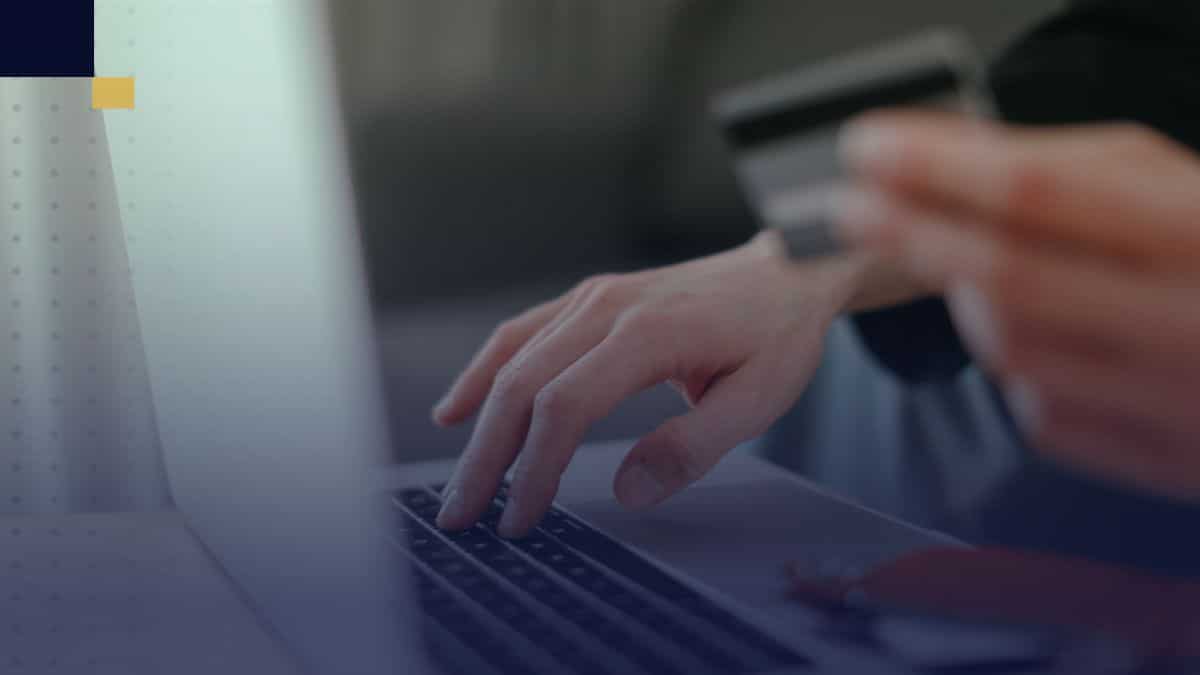 Mano de estudiante usando laptop y tarjeta de crédito para realizar un pago online de servicios académicos.