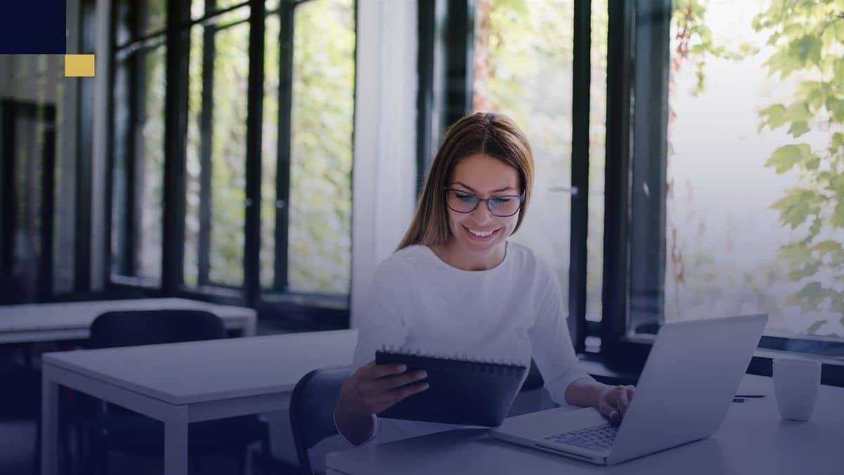 Estudiante revisando y corrigiendo su tesis en laptop con apoyo de notas en biblioteca