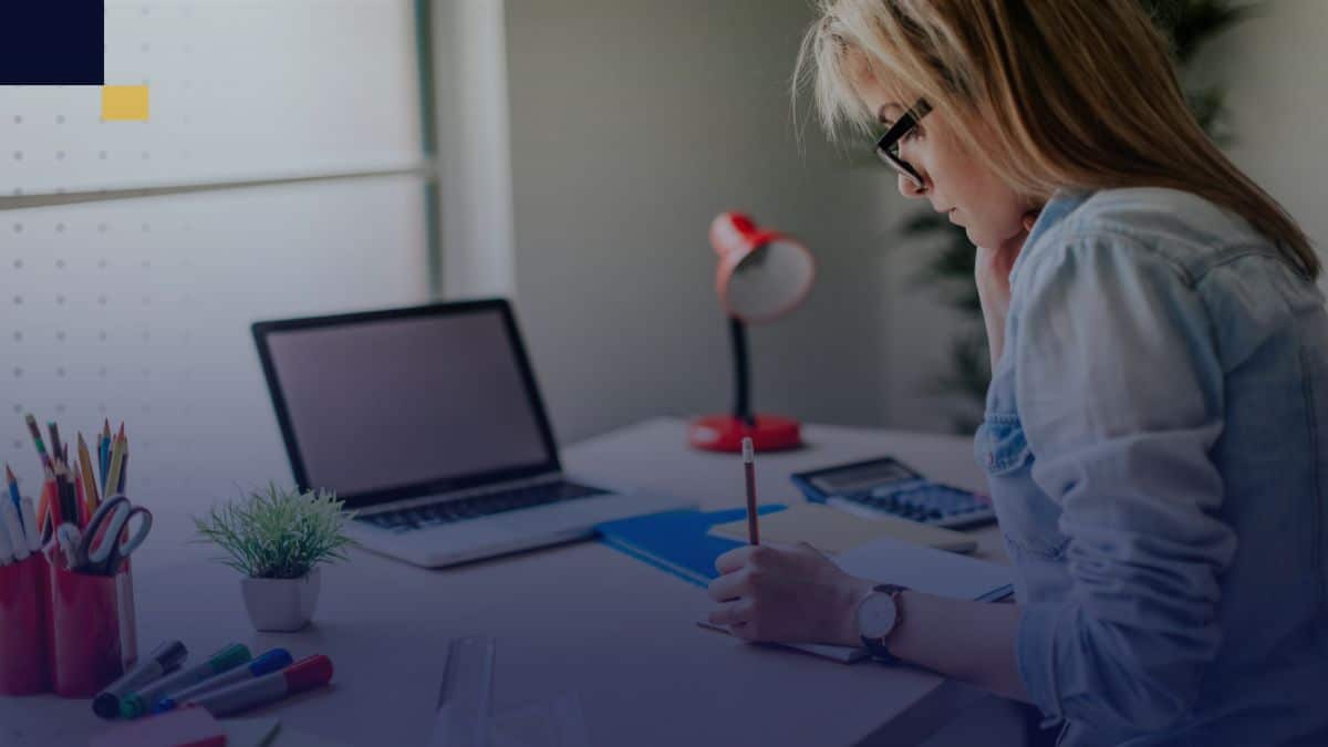 Estudiante redactando un resumen académico en escritorio con laptop y materiales de estudio