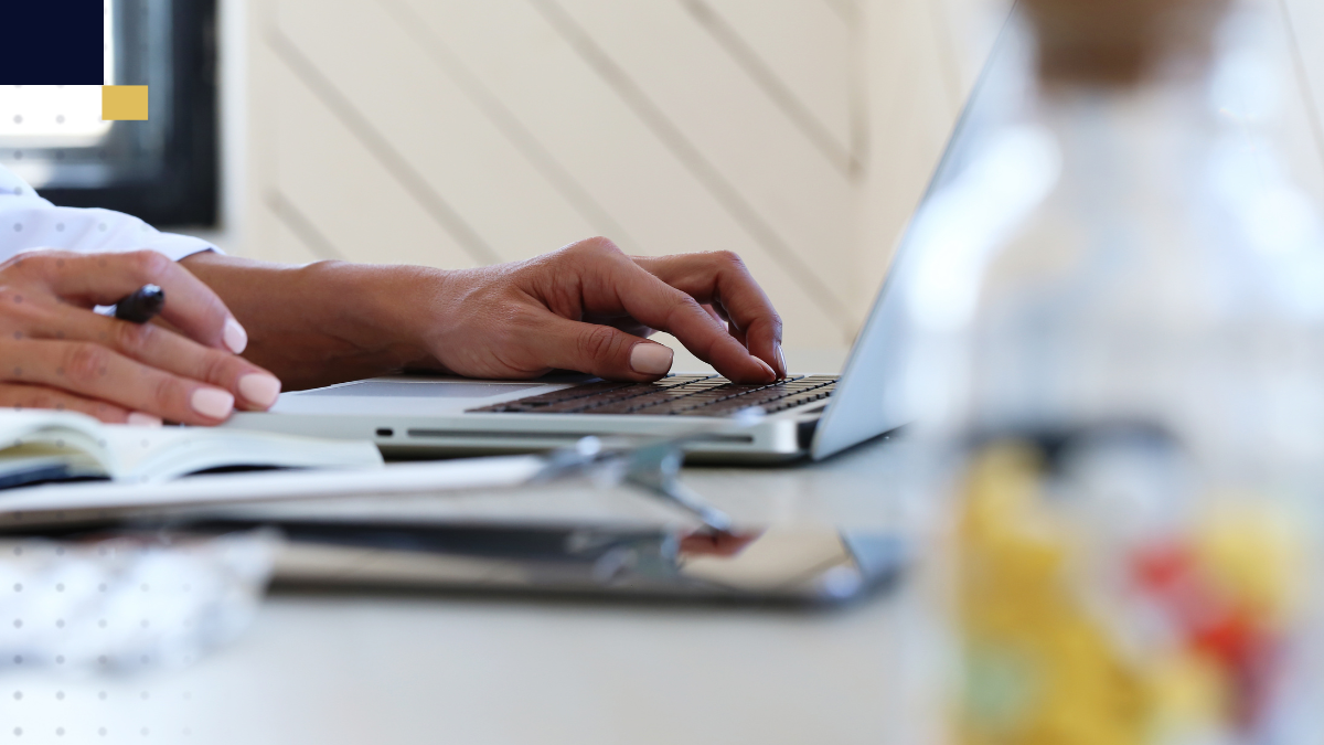 Persona redactando en laptop y tomando notas para comparar investigación descriptiva y explicativa