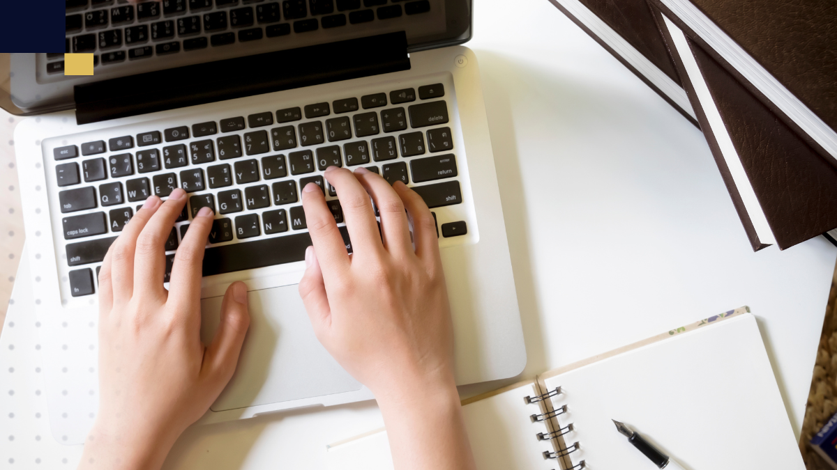 Manos escribiendo en laptop junto a cuadernos y libros para redacción de tesis con conectores académicos