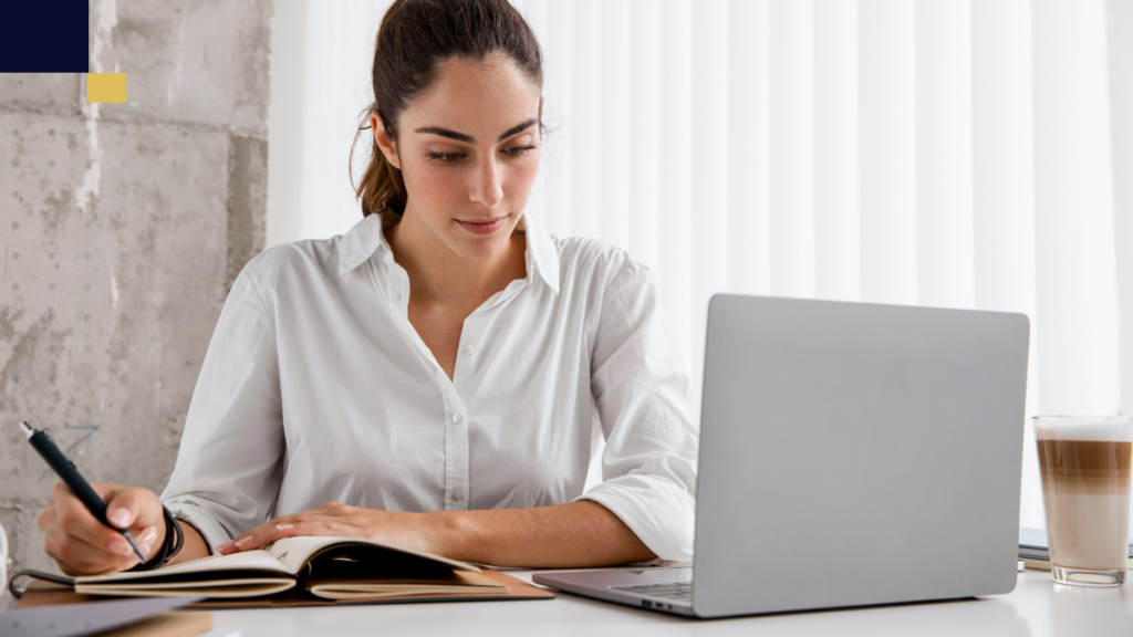 Estudiante universitaria revisando una guía impresa de Normas APA y tomando notas en laptop, aplicando la séptima edición para la redacción de su tesis.