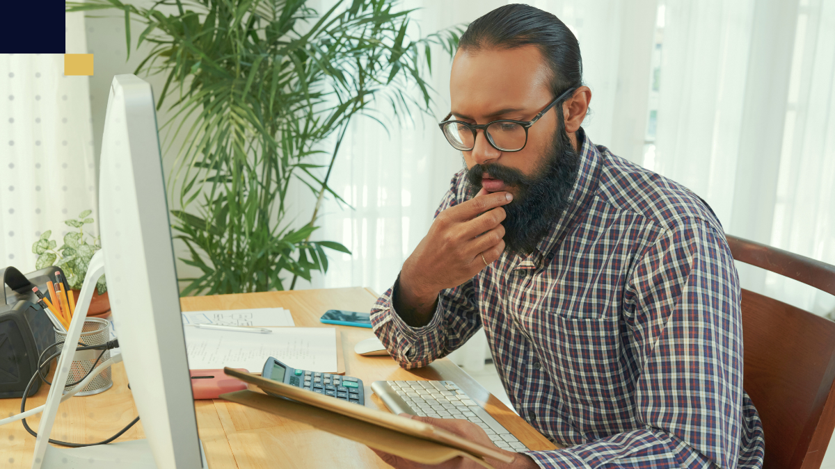 Investigador universitario trabajando en su escritorio, analizando datos en una computadora de escritorio, rodeado de materiales de oficina y plantas, en un entorno de trabajo académico.